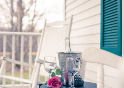 A white porch with rocking chairs and a small table holding wine.