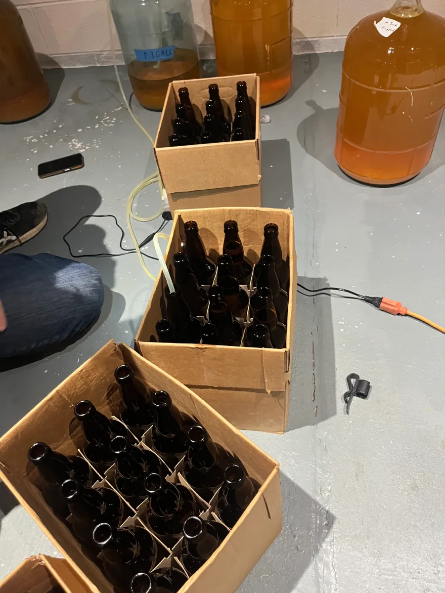 Boxes of empty bottles stacked in a basement or storage area, with some larger containers in the background.